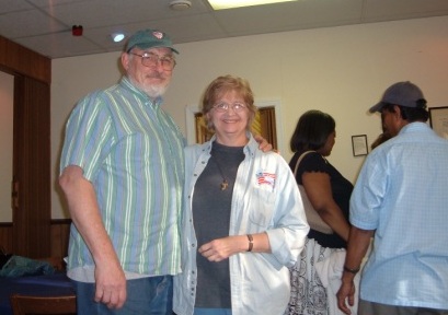 Jim and Ginny Lindsay smiling at auction fundraiser.  Jim is wearing a cap with the Episcopal shield.