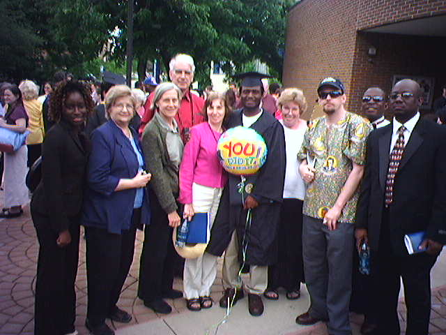 Kiombo standing with group of friends with balloon saying "you did it!"