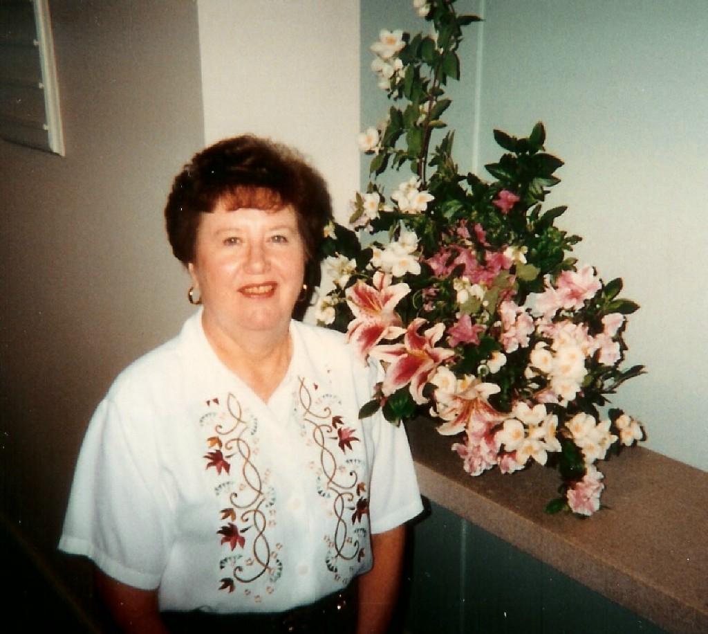 undated photo of a smiling Marlene next to altar flowers that go very well with the floral pattern on her blouse