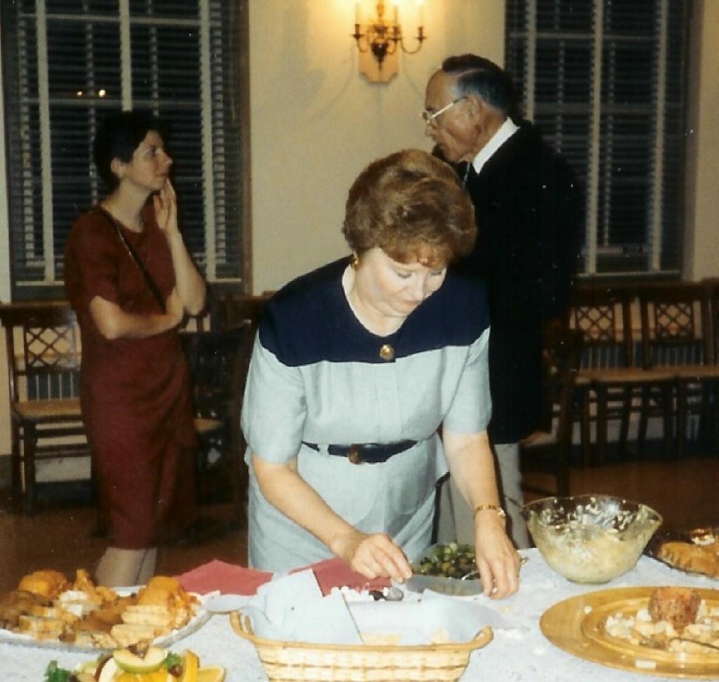 undated photo of a function in Parish Hall; Marlene is setting up a buffet and in background Rudy Hines is chatting with Elizabeth Spiers